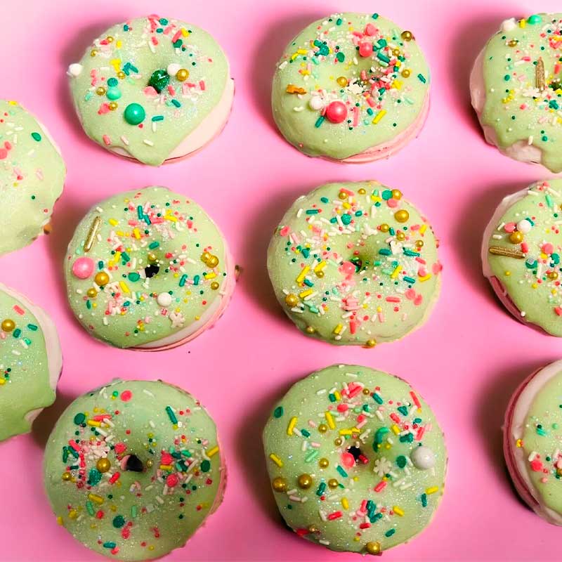 A collection of green strawberry vanilla bath bombs with colorful sprinkles on top, displayed on a pink background.
