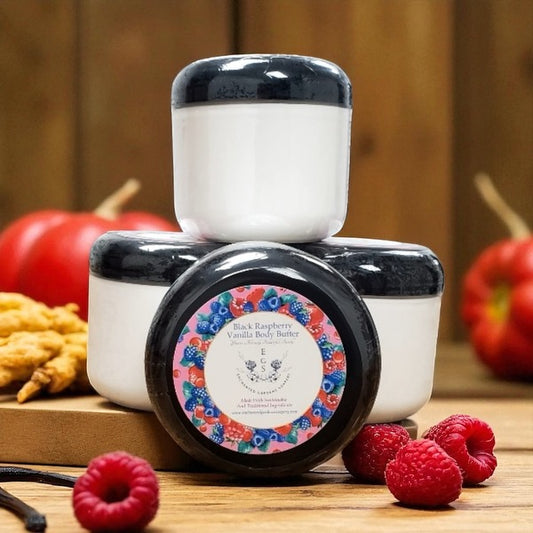 Two containers of black raspberry vanilla body butter on a wooden surface with raspberries and apples.